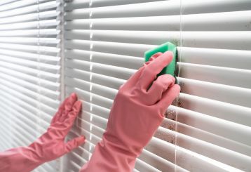 Person cleaning wooden blinds with a microfiber cloth.