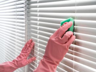 Person cleaning wooden blinds with a microfiber cloth.